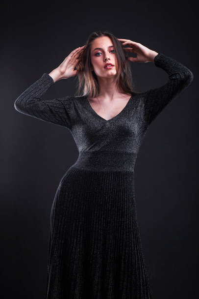 Portrait of a young beautiful woman in black tight dress on a black wall background - Φωτογραφία, εικόνα