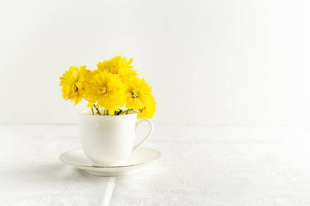 Kleiner Strauß gelber Frühlingsblumen in weißer Tasse. Horizontales Bild mit Kopierraum - Foto, Bild