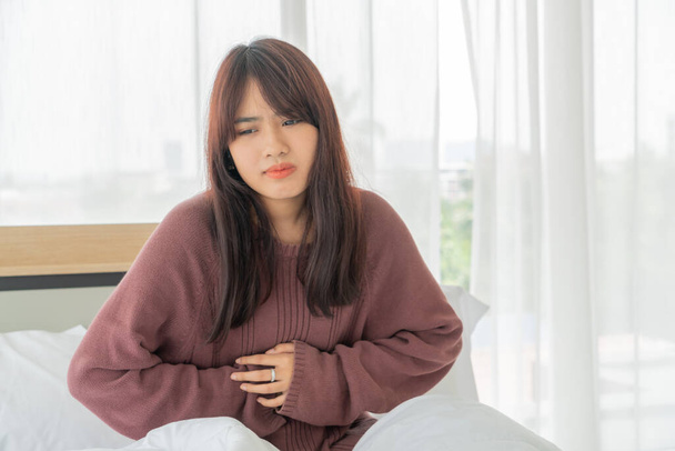 beautiful Asian women stomachache and sleeping on bed - Фото, зображення
