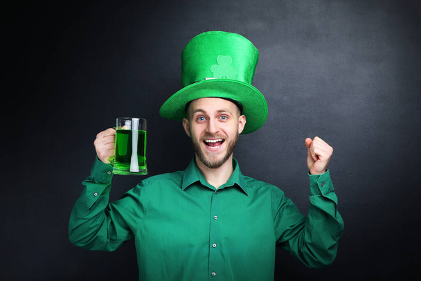 St. Patrick's Day. Young man wearing green hat with glass of beer on black background - Zdjęcie, obraz