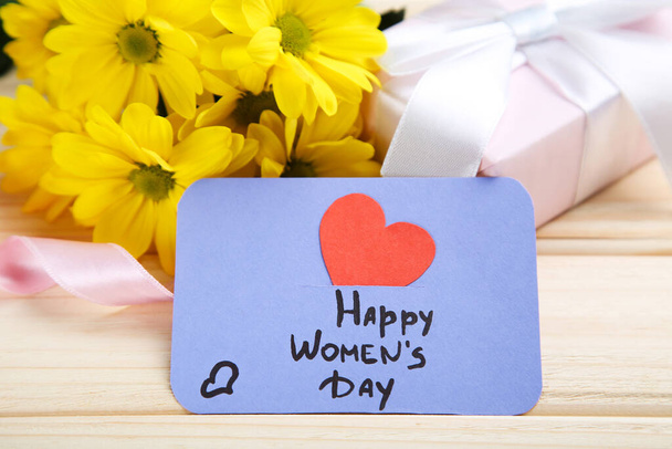 Text Happy Womens Day with chrysanthemum flowers and gift box on brown wooden background - Φωτογραφία, εικόνα