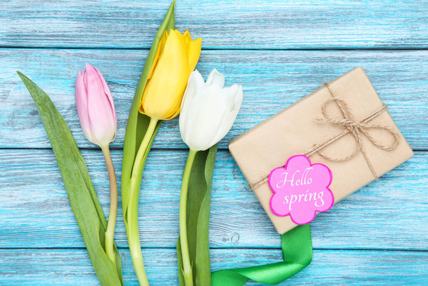 Tulip flowers with text Hello Spring and gift box on blue wooden table - Фото, изображение