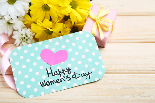 Text Happy Womens Day with chrysanthemum flowers and gift box on brown wooden background - Фото, изображение