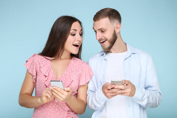 Happy young couple with mobile phones on blue background - Φωτογραφία, εικόνα