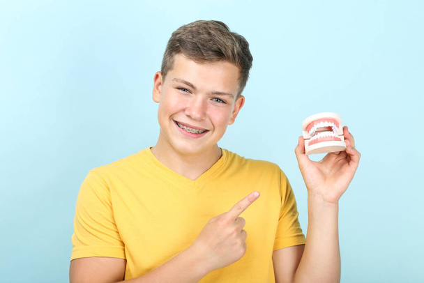 Young man with dental braces holding teeth model on blue background - Foto, Imagen