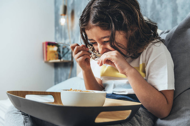 child laughing while having sunday breakfast in her parents' bed. Little girl enjoying a bowl of cereals at home in the morning, concept of healthy lifestyle and food - 写真・画像