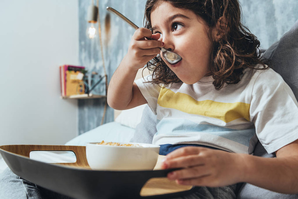 child having a sunday breakfast in her parents' bed. Little girl enjoying a bowl of cereals at home in the morning, concept of healthy lifestyle and food - Fotó, kép