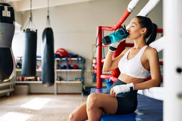 Young sporty woman drinking water after fight or workout exercising in boxing ring. Sport concept                                - Фото, изображение