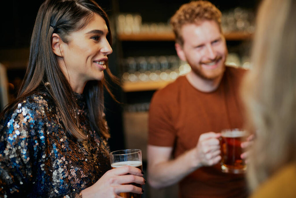 Grupo de amigos bebiendo cerveza, charlando y divirtiéndose en el pub. Noche fuera.
. - Foto, Imagen
