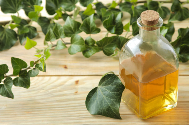 Φύλλα κισσού και σιρόπι σε ένα μπουκάλι σε ένα φυσικό ξύλινο τραπέζι. Παραγωγή αντιβηχικού φαρμάκου με εκχύλισμα κισσού. Φαρμακευτική βιομηχανία - Φωτογραφία, εικόνα