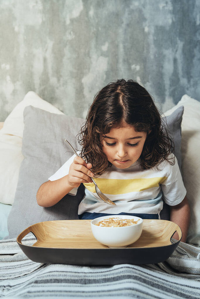 child having sunday breakfast in her parents' bed. Little girl enjoying a bowl of cereals at home in the morning, concept of healthy lifestyle and food - Фото, зображення