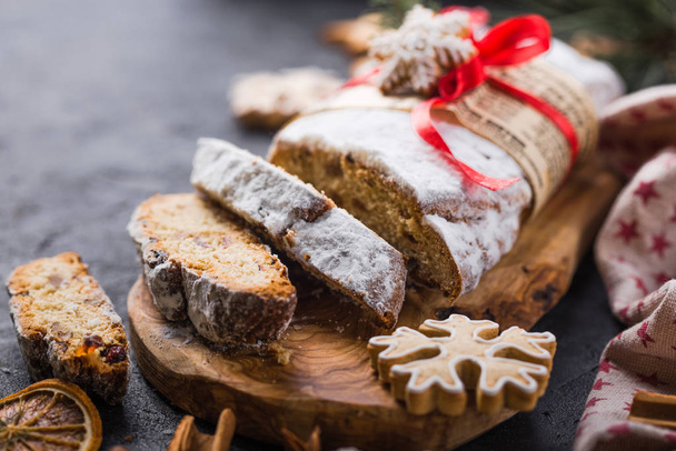 Stollene. krájený domácí vánoční dezert ukradený se sušenými bobulemi a ořechy na kamenném rustikálním stole se skořicí, pomerančovými plátky, větvemi vánočního stromku, perníčkem, selektivní zaměření - Fotografie, Obrázek