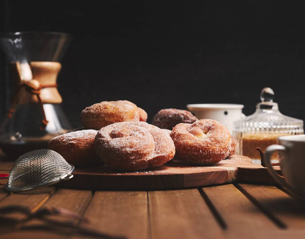 Delicious snake doughnuts with powdered sugar and chemex coffee on a wooden table with a black blurred background - Фото, зображення