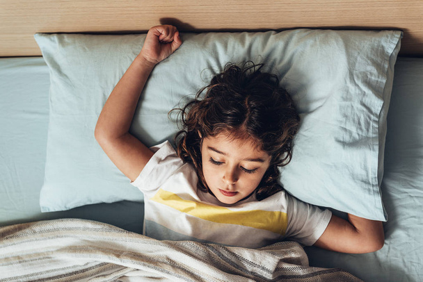 shora pohled na rozkošnou holčičku spící v posteli v dopoledních hodinách o probuzení, šťastné dětství a zdravý odpočinek koncept - Fotografie, Obrázek