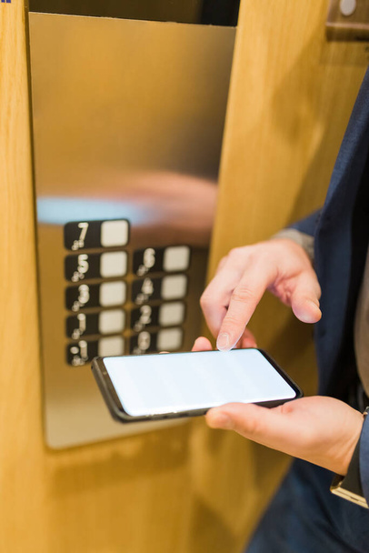Nahaufnahme eines Geschäftsmannes, der im Fahrstuhl ein Smartphone mit leerem Bildschirm benutzt. Tagungskonzept für Geschäfts- und Bürogebäude. - Foto, Bild
