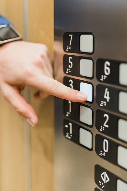 Крупный план бизнесмена, нажимающего кнопку панели управления третьего этажа в лифте
. - Фото, изображение