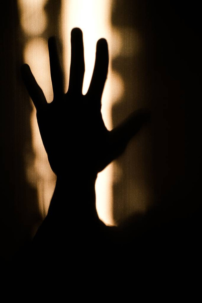 A vertical closeup shot of a hand gesture showing refusal to threat or harassment in silhouette on the wall - Φωτογραφία, εικόνα