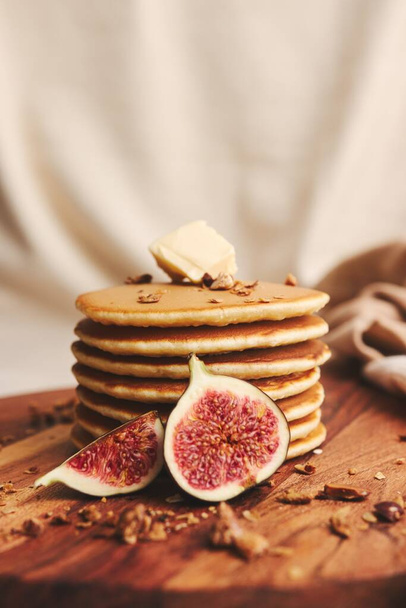 A vertical shot of pancakes with syrup, butter, figs and roasted nuts on a wooden plate - Фото, изображение