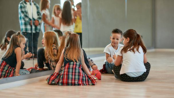 Temps de détente. Vue de l'arrière des enfants à la mode parlant entre eux tout en étant assis sur le sol et faisant une pause dans le studio de danse. Cours de chorégraphie
 - Photo, image