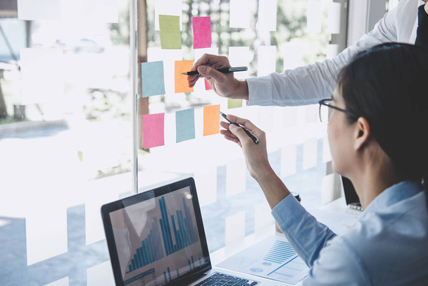 Teamwork of business team consulting market growth on financial document graph report statistics, using post it notes in glass wall to writing strategy business plan to development grow to success. - 写真・画像