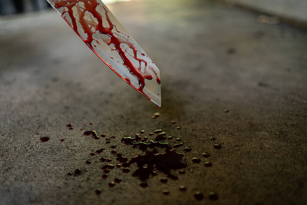 Primer plano del cuchillo con manchas de sangre y goteo en el suelo
. - Foto, Imagen