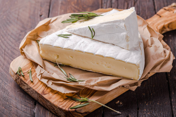 Brie sajt vagy lágy tehén szegmense - francia camembert fából készült táblán szőlővel, méhsejtekkel és diófélékkel. - Fotó, kép