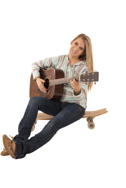 atractive woman sitting on skate board playing guitar - Fotoğraf, Görsel