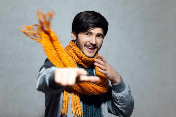 Retrato del joven hombre feliz señalando con el dedo en la cámara, usando bufanda amarilla
. - Foto, imagen