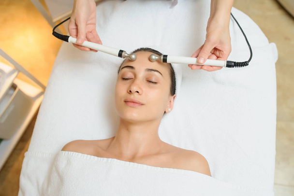  Woman facial massage spa procedure. Electric stimulation facial skin care. Microcurrent lift face. Beauty spa procedure. Anti aging rejuvenation non surgical treatment in medical interior room - Fotografie, Obrázek