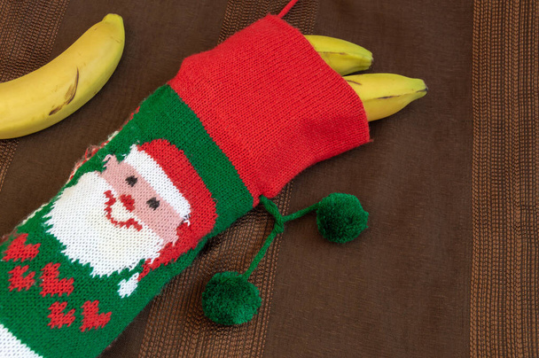 Colorful christmas sock with drawing of Santa Claus filled with bananas. Gift concept for child who has been bad, healthy gift, improvise a present... - Photo, Image