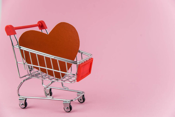 テキスト用のコピースペース付きのトレンディーなピンクの背景にショッピングカートの赤いハート。休日の概念バレンタインデーのショッピング、愛のためのお金の販売と廃棄物  - 写真・画像