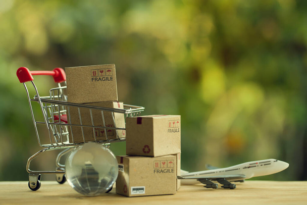 Shopping Online e e-commerce concetto: scatole di carta in un carrello della spesa e globo di cristallo, aereo. Negozi online sono considerati come un altro mezzo di scambio di beni tra imprenditori e clienti. - Foto, immagini