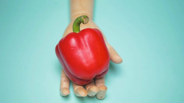 wooden hand holds red bell pepper. blue background - Photo, Image