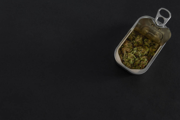 Dose mit qualitativ hochwertigen Marihuana-Knospen isoliert auf schwarzem Hintergrund mit Kopierraum links. Verpacktes Marihuana. Offene Aluminiumbox mit Unkraut im Inneren. - Foto, Bild