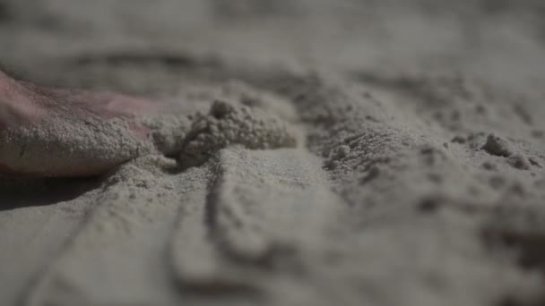 Um tiro de perto na mão de um homem a tocar na praia de areia. Movimento lento vida real
 - Filmagem, Vídeo