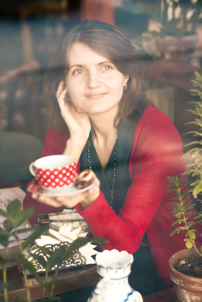 mujer rubia joven con taza de té retrato a través de la ventana de la cafetería foto de cerca
 - Foto, imagen