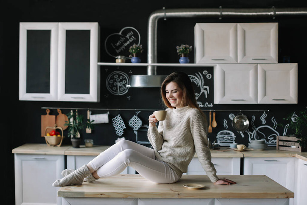 A girl drinking coffee in the kitchen at home. Young woman holding cup of coffee.  Girl drinking beverage in cafe. Good morning.  - Foto, afbeelding