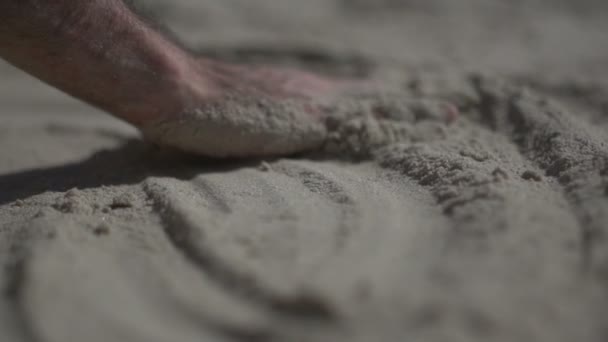 Um tiro de perto na mão de um homem a tocar na praia de areia. Movimento lento vida real
 - Filmagem, Vídeo