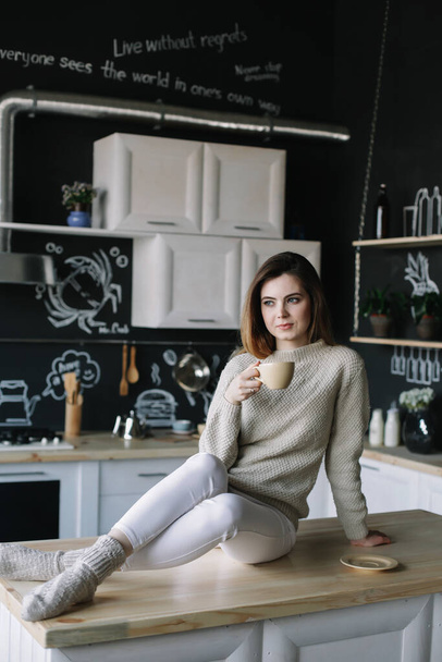 A girl drinking coffee in the kitchen at home. Young woman holding cup of coffee.  Girl drinking beverage in cafe. Good morning.  - Фото, изображение