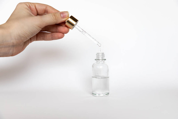 Krople kwasu hialuronowego spadają z pipety kosmetycznej na białym tle, Mock-Up butelki szkła kroplomierz - Zdjęcie, obraz