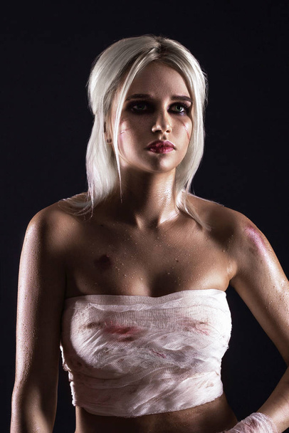 Beautiful young white-haired warrior girl with bandage on hands in light underwear on dark background. Portrait of a cute girl with a scar in white lingerie - Foto, imagen
