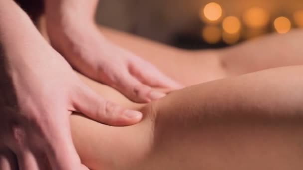Primer plano del masaje premium anti-celulitis en el muslo. Las manos masculinas hacen masaje de bienestar del muslo a la niña paciente en un acogedor estudio con poca luz. Servicios de masajes de lujo
 - Metraje, vídeo