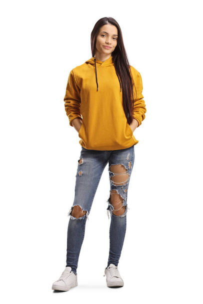Full length portrait of a young female with long black hair, yellow hoodie and ripped jeans isolated on white background - Photo, image