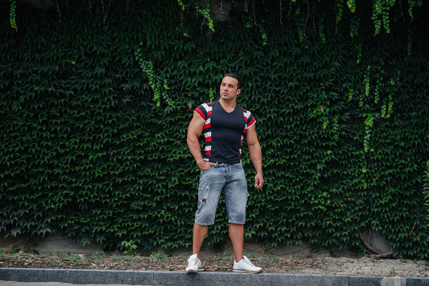 A sporty guy is sitting near a green wall of plants. Ecology - Photo, Image