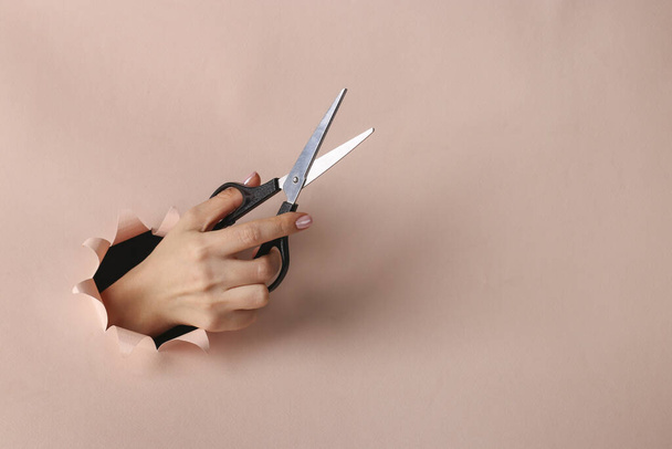 Tijeras de mano hembra sosteniendo a través de agujero redondo en papel rosa, espacio de copia
 - Foto, imagen