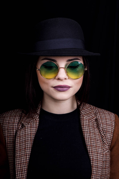 Hermosa chica en sombrero y gafas redondas está posando en Studio sobre fondo negro
 - Foto, imagen