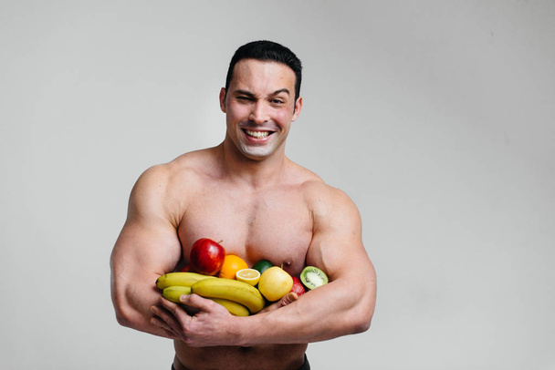 Sporty sexy guy posing on a white background with bright fruits. Diet. Healthy diet - Foto, Imagen