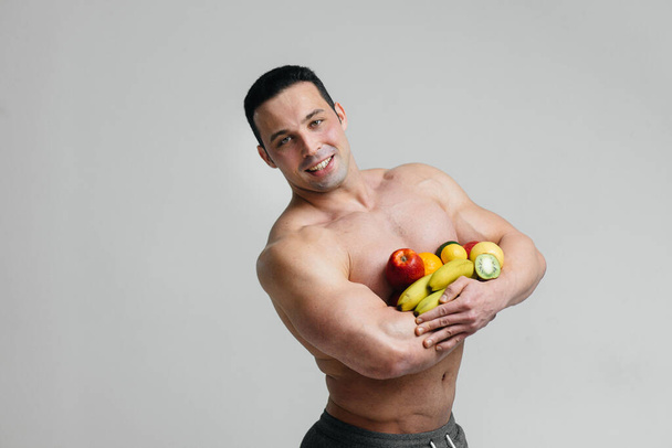 Sporty sexy guy posing on a white background with bright fruits. Diet. Healthy diet - Foto, Imagen