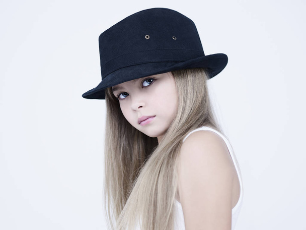 little pretty girl in black classic hat. Studio ashion photography of kid in white dress. Beautiul model on white background. - Photo, image