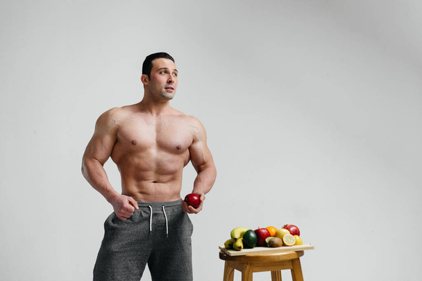 Sexy wegańskie facet z nagim tułowia pozowanie w studio obok owoców. Dieta. Zdrowa dieta - Zdjęcie, obraz